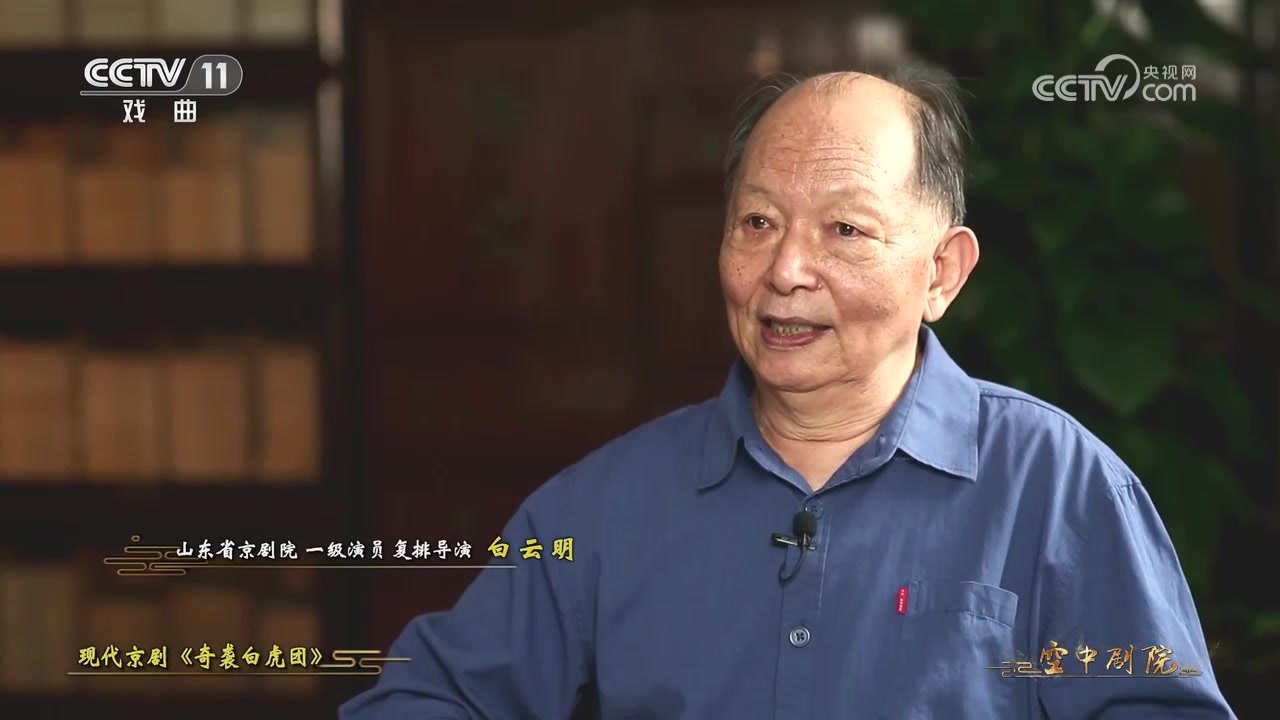 白云明受访截帧：画面左下姓名条作「山东省京剧院一级演员　复排导演　白云明」，题条作「现代京剧《奇袭白虎团》」