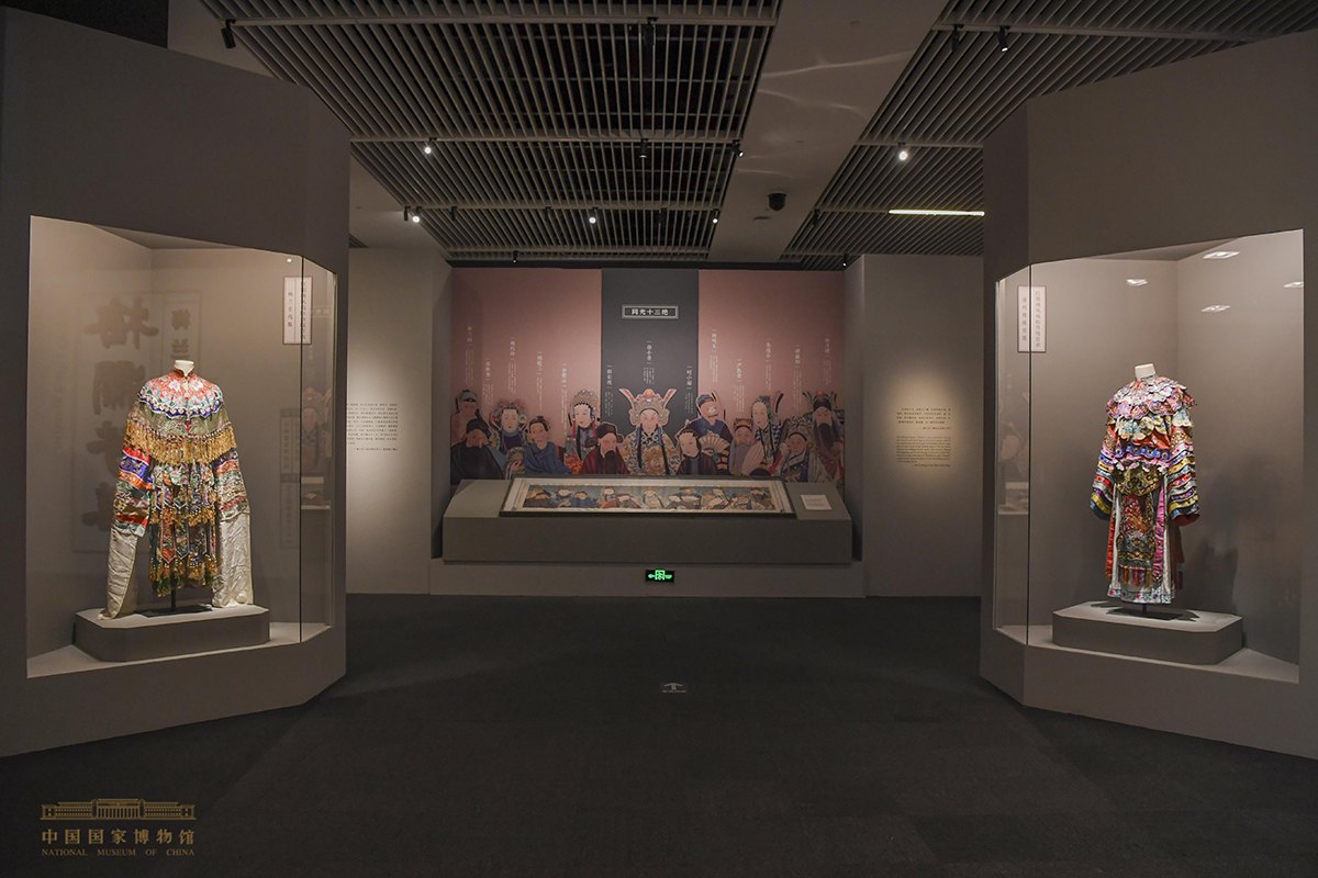 中国国家博物馆“梅澜芳华——梅兰芳艺术人生展”“同光十三绝”展区（正面墙放大《同光十三绝》群像，中央展柜平置长卷，两侧陈列戏衣；展厅现场照片，非程长庚本人影像）