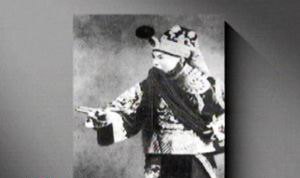 京剧老生剧照（头戴缀绒球盔头、挂白色长髯、深蓝绣云纹戏服、白色水袖，作指点身段）；取自央视《跟我学》「前四大须生——高庆奎」页内配图，原页无题注故不指认剧目（已裁去左下角CCTV.com水印）