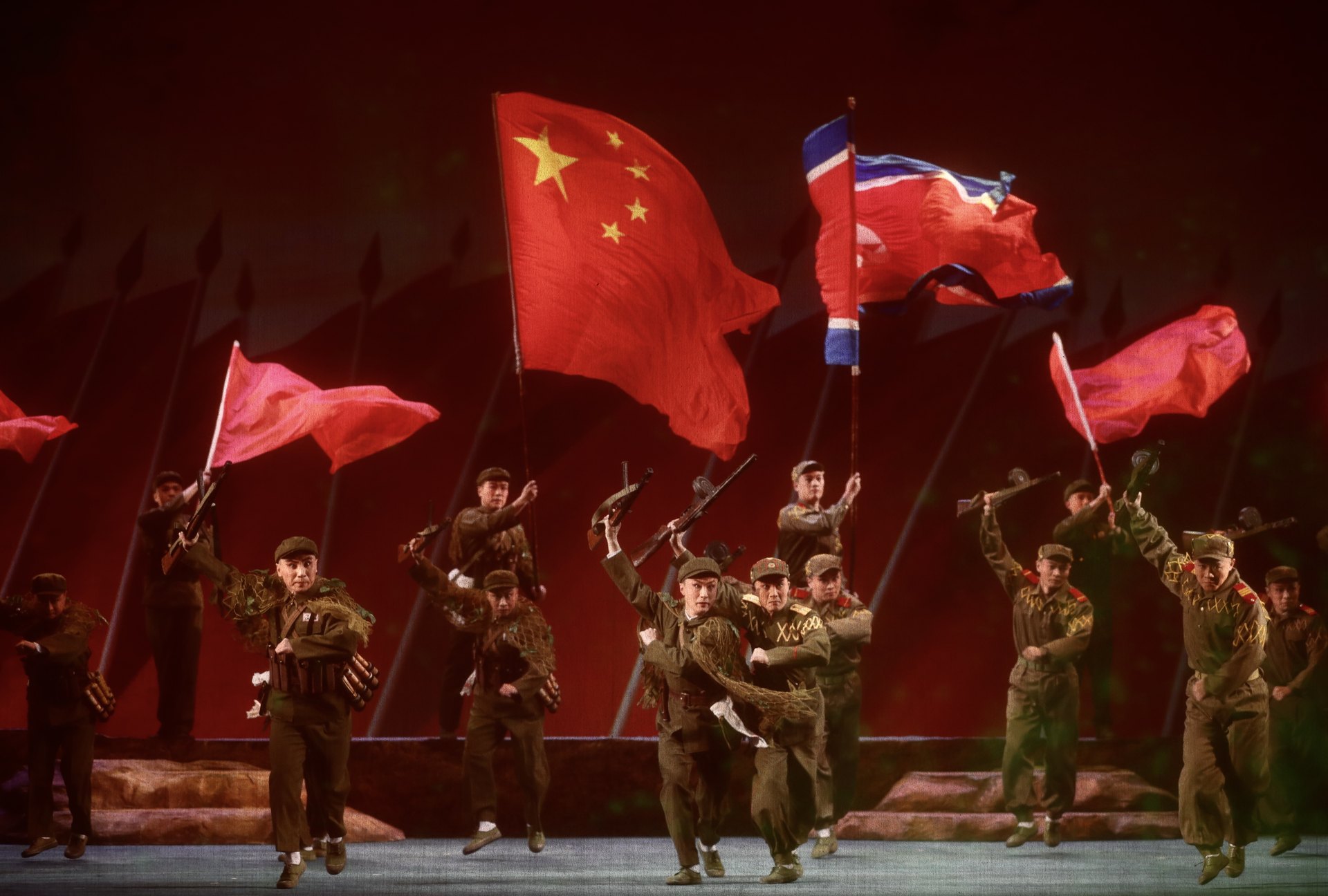 现代京剧《奇袭白虎团》剧照：中国人民志愿军战士持枪群像与中朝两国国旗（2020年纪念中国人民志愿军抗美援朝出国作战70周年舞台艺术优秀剧目展演开幕演出）