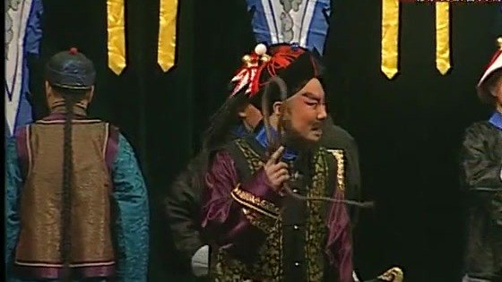 京剧《廉吏于成龙》演出照：公堂／官场场面——官服人物居中，差役背身侍立，台口悬蓝黄旗帜