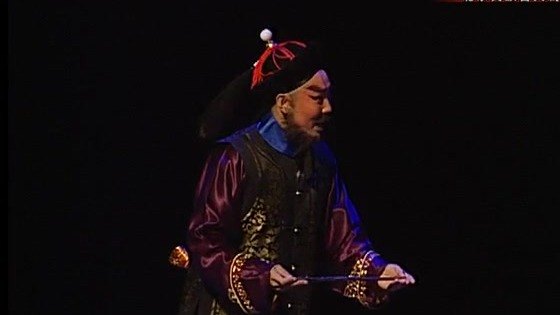 京剧《廉吏于成龙》演出照：官服人物（乌纱官帽、黑三髯，手持折扇）念白一节