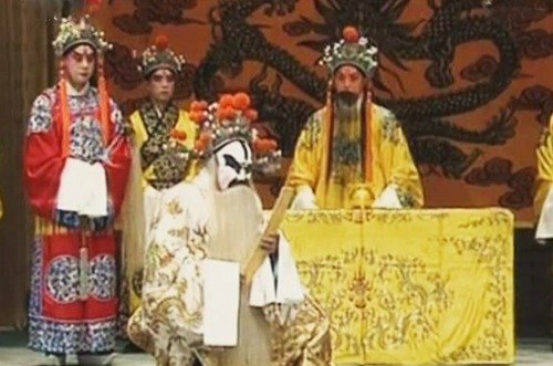 京剧《打金砖》剧照：金殿一场，御案后帝王扮相者（俊扮、黄蟒、黑髯）端坐，白面净角跪陈于前，旁有俊扮角色持笏侍立（央视网《京剧音配像〈打金砖〉》文内所载）
