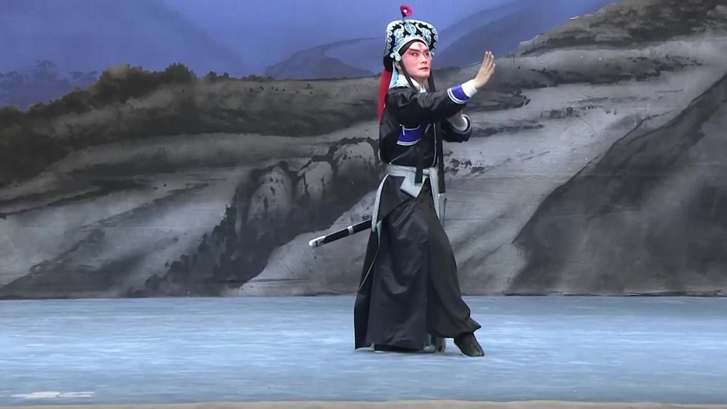 央视《中国京剧像音像集萃》20230915《林冲夜奔》演出影像截帧：黑箭衣、红绒球罗帽的林冲在山水天幕前亮相