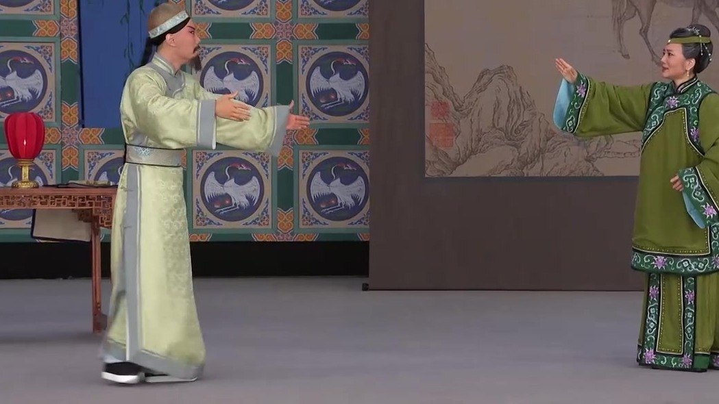 京剧《瘦马御史》演出照：老生（浅豆绿褶袍、髯口）与旦角对戏，舞台设桌灯、鹤纹屏与山水画屏