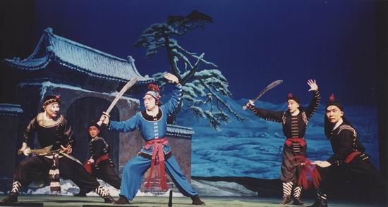 京剧《野猪林》剧照：雪夜覆雪山门与雪地松树，林冲（武生俊扮）持刀与众角色开打（国家京剧院官网剧目页所载）